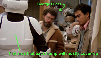 screencap from the Making Magic Archive CD which highlights behind the scenes image of a Biker Scout costume being fitted and reviewed by George Lucas.  This image clearly shows the back of the scout costume without the back hump attached.    You  can clearly see teh flat panel that gets covered by the back hump